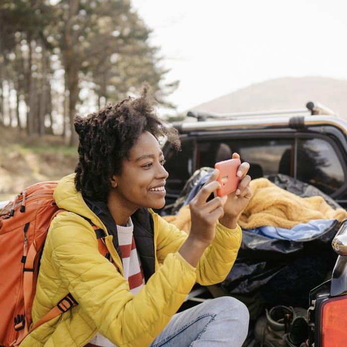 A camper uses her phone to take a picture from the back of a pickup truck filled with camping gear.